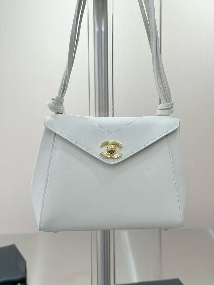 A white leather shoulder bag with a gold-tone interlocking CC logo clasp, hanging from a metal display stand.