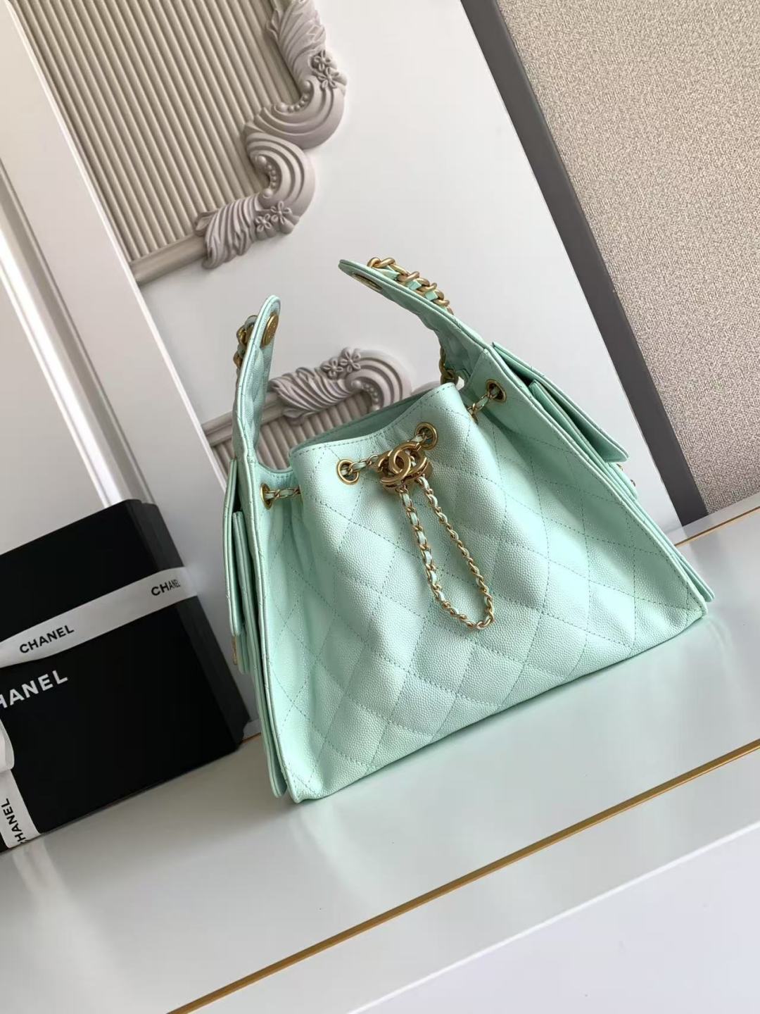 Mint green handbag with gold chain on a white surface, with Chanel branding in the background.
