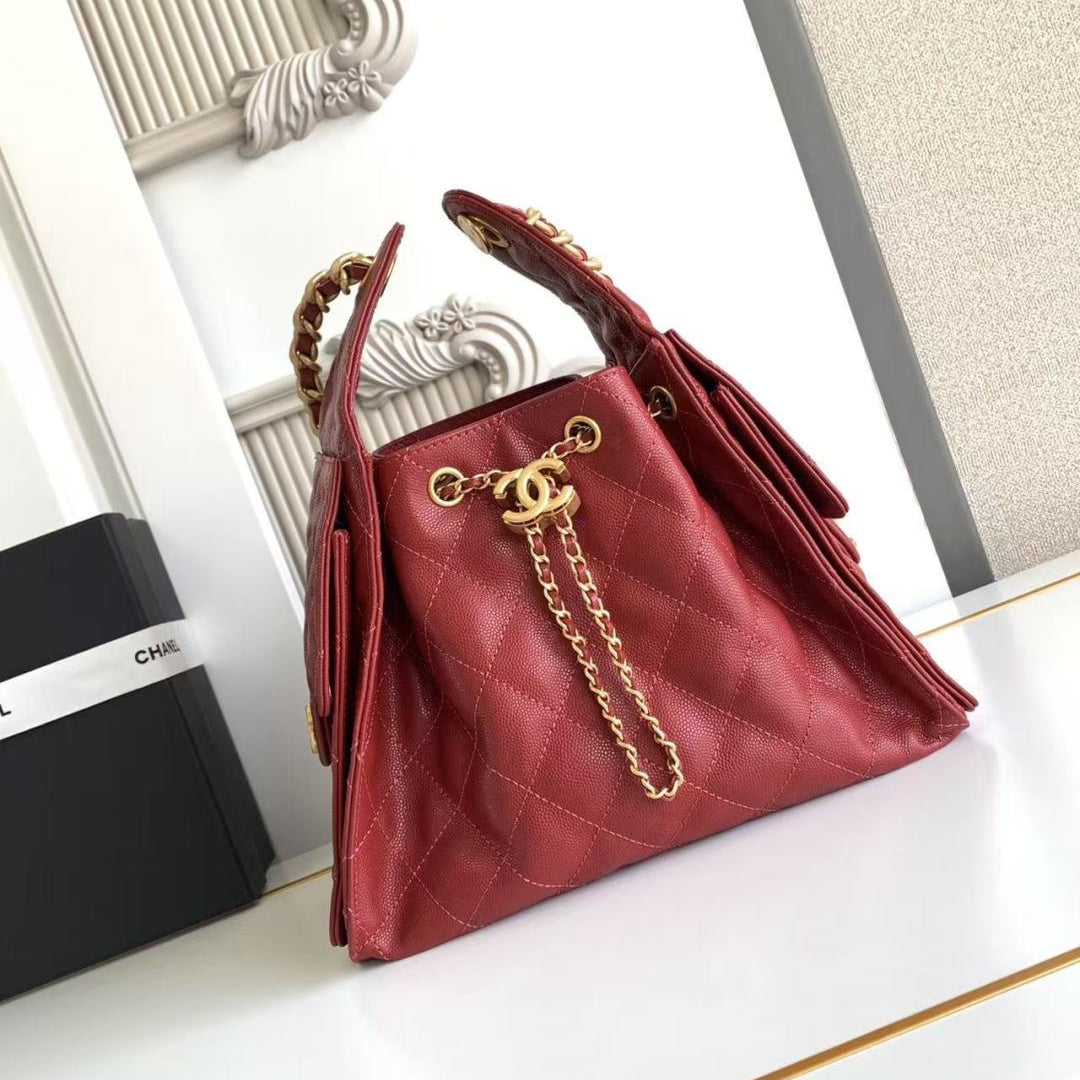 A red quilted leather handbag with gold-tone hardware and a chain strap, displayed on a white surface next to a black Chanel box.