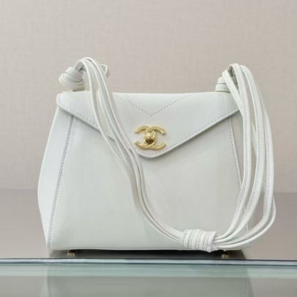 A white leather shoulder bag with a gold-tone interlocking CC logo, resting on a reflective glass surface against a light beige background.