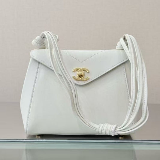 A white leather shoulder bag with a gold-tone interlocking CC logo, resting on a reflective glass surface against a light beige background.
